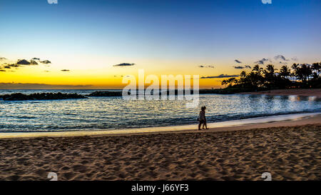 Paare, die bei Sonnenuntergang am Strand von Honu Lagune, die 2. Lagune und den Pazifischen Ozean mit bunten Sky at Ko Olina an der Westküste von Oahu Stockfoto