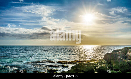 Sonnenuntergang über dem Horizont mit ein paar Wolken an der felsigen Küste Paradise Cove an der Westküste von der tropischen hawaiianischen Insel Oahu Stockfoto