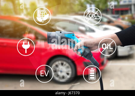 Luftverschmutzung und Gewächshaus-Gas-Emissionen-Konzept reduzieren. Hand halten Ladestation Fahrzeug Elektroauto und Symbole mit Weichzeichnen Autos Hintergrund. Stockfoto