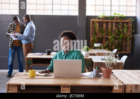 Lächelnde afrikanische Geschäftsfrau, die Arbeiten an einem Schreibtisch Stockfoto