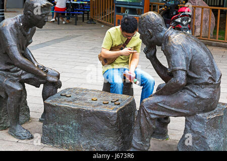 Chinesischer Mann auf dem Handy neben Statuen, Yinchuan, Ningxia, China Stockfoto