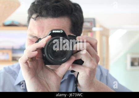 Mann mit schwarzen Haaren und blauen Shirt fotografieren Selbstporträt in einem Spiegel im Inneren eines Hauses Stockfoto