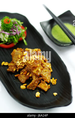 Sautierte Schweinefleisch mit Erdnüssen und Salat auf schwarzem Teller Stockfoto