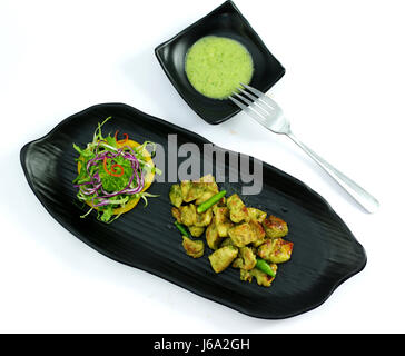 Geschmortes Schweinefleisch mit Chili-Sauce und Salat auf schwarzem Teller Stockfoto