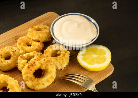 Ein Foto von Calamari Ringe mit einer Scheibe Zitrone und Ali-Oli-Soße, auf einem schwarzen Hintergrund mit einem Platz für text Stockfoto