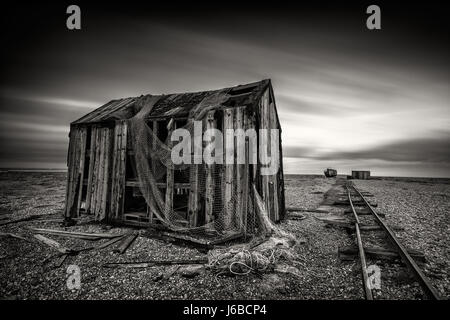 Fischerhütte auf einem Kiesstrand mit Langzeitbelichtung Wolken in Monochrom aufgegeben. Dungeness, England Stockfoto