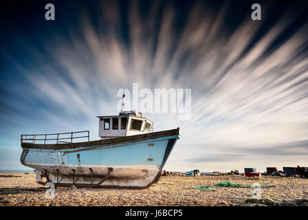 Altes Fischerboot auf einem Kiesstrand mit Langzeitbelichtung Wolken aufgegeben. Dungeness, England Stockfoto