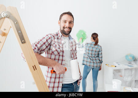 Home Makeover und Renovierung: junges Paar redecorating ihr neues Haus und Malerei Wände, der Mann ist auf einer Leiter gelehnt und posiert Stockfoto