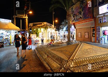 Blick auf den Roman Sarakino Brunnen entlang der Uferpromenade in der Nacht mit Souvenirläden auf der Rückseite, Hersonissos, Kreta, Griechenland, Europa. Stockfoto