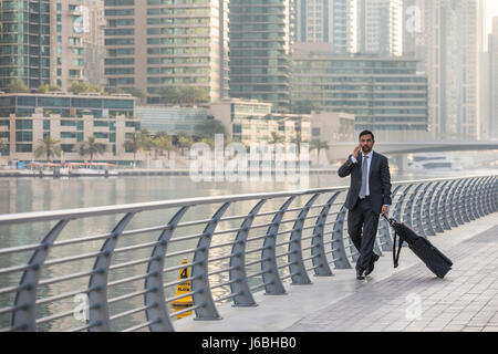 Geschäftsmann mit einem Koffer sprechen Ona Telefon in der Dubai Marina, Vereinigte Arabische Emirate Stockfoto