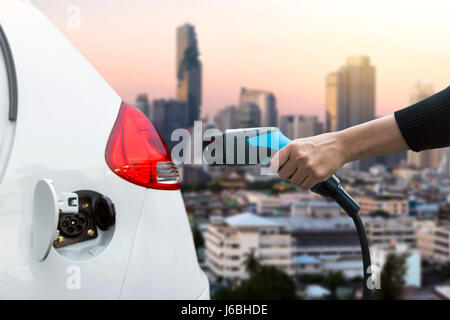 Luftverschmutzung und Gewächshaus-Gas-Emissionen-Konzept reduzieren. Hand halten und laden Elektro-Auto mit Unschärfe Stadt Ansicht Hintergrund. Stockfoto