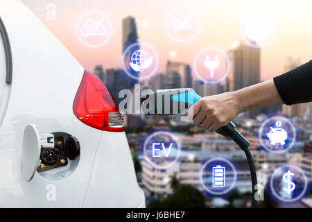 Luftverschmutzung und Gewächshaus-Gas-Emissionen-Konzept reduzieren. Hand halten und laden Elektro-Auto mit Unschärfe Stadt Ansicht Hintergrund. Stockfoto