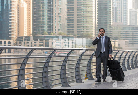 Geschäftsmann mit einem Koffer an einem Telefon in der Dubai Marina, Vereinigte Arabische Emirate Stockfoto