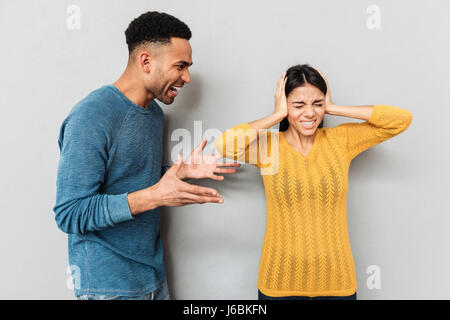 Afrikanischen aggressiven Mann schreien an seine Frau während sie schließen Ohren über grauen Hintergrund isoliert Stockfoto