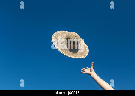 Die weibliche Hand wirft einen Strohhut. Blue Sky ist im Hintergrund. Stockfoto