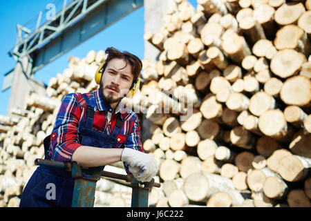 Portrait der Mann trug Ohrenschützer Blick in die Kamera während der Arbeit an Holz schneiden Website Stockfoto