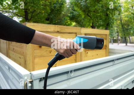 Luftverschmutzung und Gewächshaus-Gas-Emissionen-Konzept reduzieren. Hand halten und laden Elektro-Auto mit Logistik LKW Auto und Grün Natur Blick backgr Stockfoto