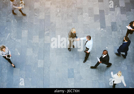 Von oben zwei Erwachsenen Geschäftsleute traf Händeschütteln im Büro Halle mit Arbeiter herumlaufen. Stockfoto
