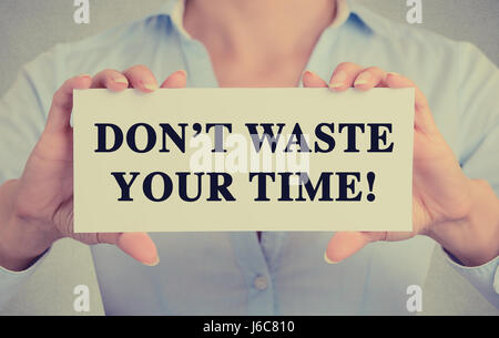 Geschäftsfrau Hände weiße Karte mit Namensschild vergeuden Sie nicht Ihre Zeit Text Nachricht auf graue Wand Büro Hintergrund isoliert. Retro-Instagram Stil ima Stockfoto