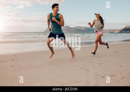 Schuss von Fitness-paar am Strand laufen. Glückliche junge Mann und Frau Läufer am Ufer Meeres. Stockfoto