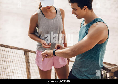 Junges Paar mit tragbarer Technologie während des Trainings. Junger Mann zeigt Herzfrequenz-Monitor Watch Frau während der Pause. Stockfoto