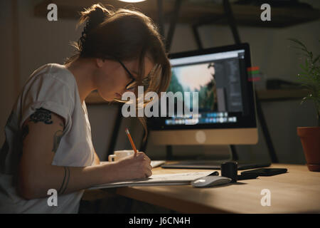 Foto der jungen Frau Designer sitzen drinnen bei Nacht Zeichnung skizziert im Album mit Computer. Stockfoto