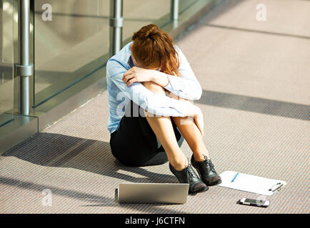 Closeup Portrait junge depressiv, traurig gestresst, Weinen Geschäftsfrau auf Boden in einem Saal des corporate building, Firmensitz, sitzend über ihre Fa Stockfoto