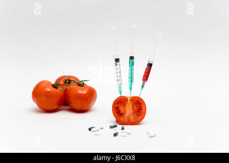 GVO-Konzept auf weißem Hintergrund mit Spritzen, Tabletten und Tomaten. Stockfoto