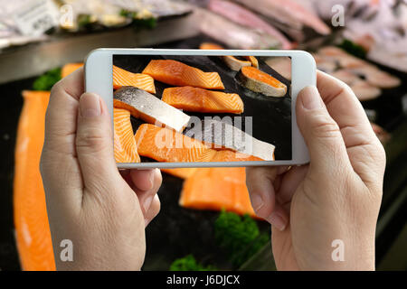 Selective Fokus auf Handy-Bildschirm, Hand Holding Smartphone und Stücke von frischem rohen Lachs Fisch Filets auf mobile Leinwand im Frischmarkt Stockfoto