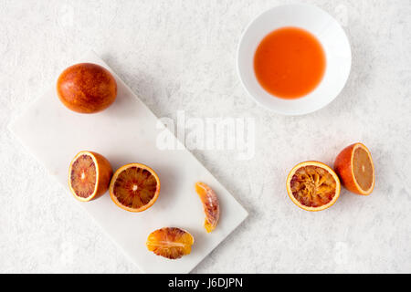 Ganz, halbiert und gepressten Blutorangen und frischen Saft auf weißem Marmor, hacken, Brett und weiß strukturiert marmorierten Hintergrund mit Textfreiraum. Stockfoto