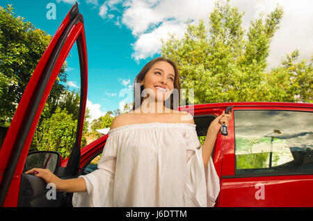 Schöne junge Frau hält ihre Schlüssel und lächelnd in der Nähe ihrer eigenen roten Auto Stockfoto