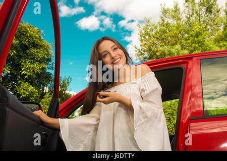 Schöne junge Frau hält ihre Schlüssel und lächelnd in der Nähe ihrer eigenen roten Auto Stockfoto