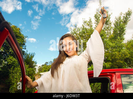 Schöne junge Frau zu öffnen, halten Sie ihre Schlüssel und lächelnd in der Nähe von ihrem roten Auto Stockfoto