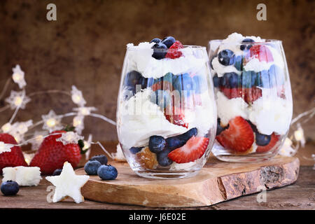 Trifle mit Heidelbeeren, Erdbeeren, Schlagsahne und Sterne geformte Sandkuchen gegen einen rustikalen Hintergrund gemacht. Perfekt für vierten Juli. Flache Stockfoto