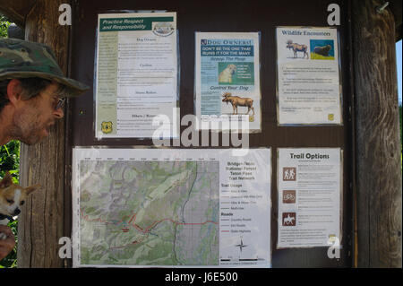 Mann halten Hund von der Seite betrachtet eine Teton Pass Trail Netzwerk und Umweltschutz Infotafel, Teton Pass Wahlbeteiligung, Wyoming, USA Stockfoto