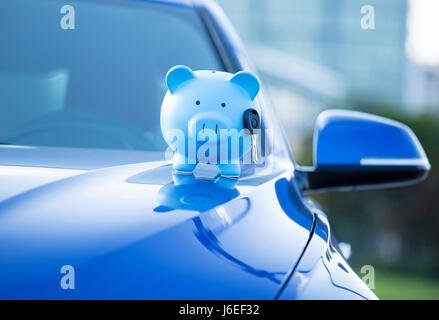 Closeup abgeschnitten Bild blau Neuwagen mit Sparschwein und Schlüssel auf Motorhaube, isoliert außerhalb Firmengebäude. Autohaus bietet Kreditlinie Finanzen servi Stockfoto