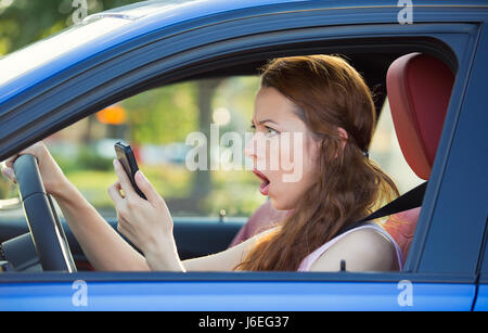 Closeup Portrait junge schockiert, betonte Frau Fahrer, fahren im Auto Check-Smartphone genervt von schlechter Text Nachricht e-Mail isoliert außerhalb Straße Stockfoto