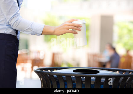 Closeup abgeschnitten Bild Frau Hand werfen leere Kaffee Pappbecher in Recyclingbehälter, außen isoliert Bäume Hintergrund. Recycling, Eco freundliche appro Stockfoto