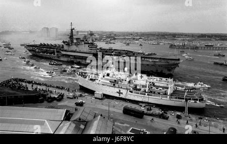 AJAXNETPHOTO. 21. JULI 1982 - PORTSMOUTH, ENGLAND. - HERMES KEHRT NACH IHREM EINSATZ IM SÜDATLANTIK FÜR DIE FALKLAND-INSELN-KAMPAGNE ZU EINER MITREISSENDEN BEGRÜSSUNG ZURÜCK. BEREITS IM VORDERGRUND LIEGT DIE HMS HECLA (A133), EINES VON MEHREREN UNTERSUCHUNGSSCHIFFEN, DIE ALS KRANKENHAUSSCHIFFE IM KONFLIKT EINGESETZT WURDEN. FOTO: JONATHAN EASTLAND/AJAX. REF:820721 3 4 Stockfoto