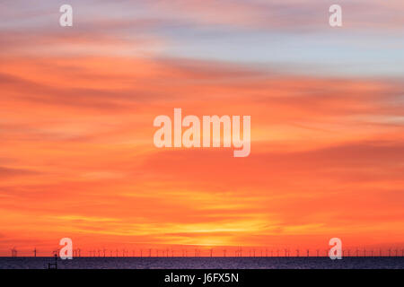 Orange Dämmerung Himmel über den Thanet Offshore Windpark, bei der die Zeile der Turbinen onon am Horizont. Windenergieanlagen Silhouette gegen den hellen orange sky. Stockfoto