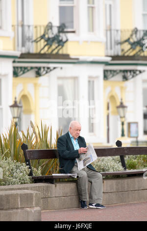 Ein Mann sich Zeit nehmen, die Morgenzeitung auf Llandudno Promenade vor der vielen bunten Hotels und Pensionen in Nord-Wales zu lesen Stockfoto