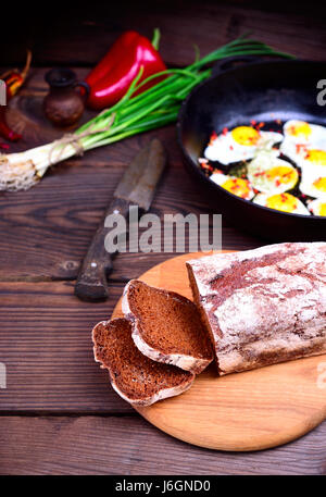 In Scheiben Roggenbrot auf ein Schneidebrett Küche hinter Spiegeleier in einer Pfanne erhitzen Stockfoto