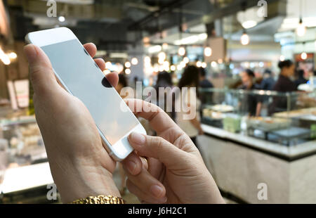 Hand mit Handy und abstrakt verwischen schöne Luxus-Food-Court im Einkaufszentrum und Retail Store Interieur für Hintergrund Stockfoto