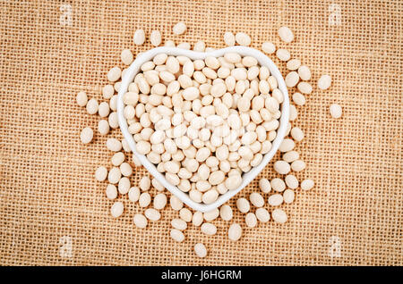 Weiße Bohnen Samen in Whtie Schale auf Sackleinen Hintergrund. Stockfoto
