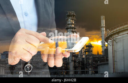 Industrie 4.0-Konzept. Doppelbelichtung Hand Holding Smartphone und automatisieren Sie mit Öl-Raffinerie-Industrie Sonnenuntergang Hintergrund Stockfoto