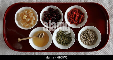 Stichprobe von gesunden Lebensmitteln in weißen Schalen auf einem roten Tablett. Stockfoto