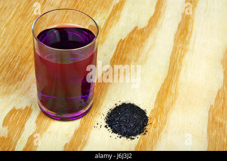 Haufen von Kaliumpermanganat-Kristalle und Glas Wasser auf einem Holztisch Stockfoto