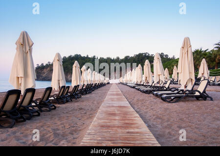 Reihe von Sonnenschirm Sonnenschirme am Strand. Ruhigen Blick auf das Mittelmeer. Erstaunliche rosa Sonnenaufgang mit klarem Himmel. Ort: Türkei, Kemer. Stockfoto