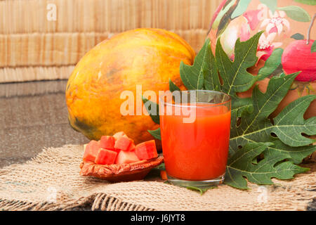 Frische Papaya-Saft in das Glas mit Papaya-Früchte, Papaya Blatt- und Papaya Scheiben auf Sackleinen auf dem Hintergrund einer Strohmatte und ein Ton-Topf Stockfoto