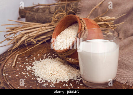 Vegane Sesammilch im Glas und weißen Sesam in einem Tontopf auf einem Holztisch. Rohkost-Ernährung. Horizontale Foto ohne Menschen für Katalog, Menü, b Stockfoto